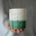 Manos sosteniendo vaso cerámica artesanal Stand By Me verde y blanco hecho a mano 230ml - Maia Artesanía Cerámica