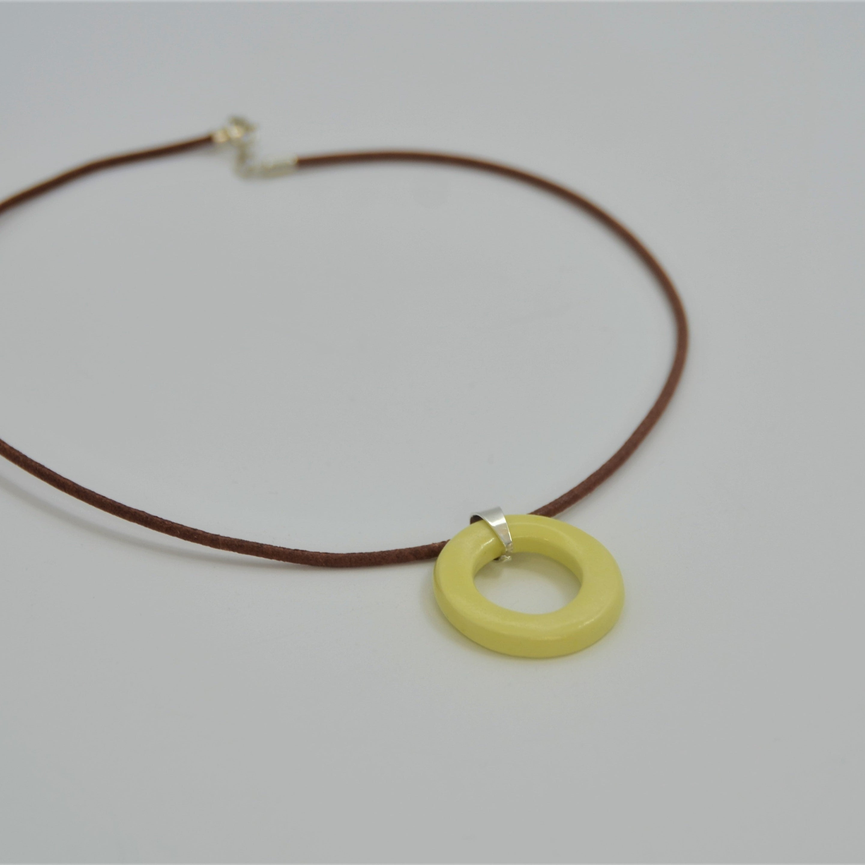 Colgante de cerámica circular amarillo sobre superficie natural, joyería artesanal única de Maia Cerámica