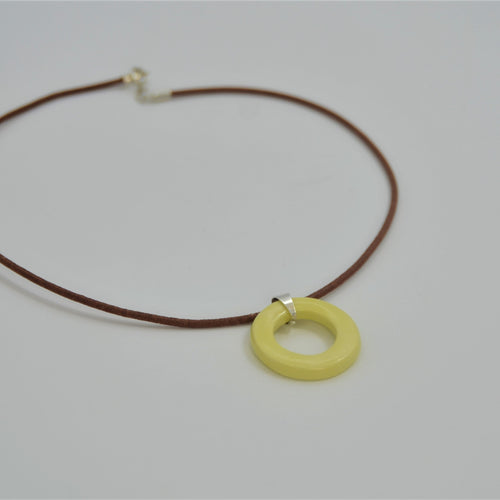Colgante de cerámica circular amarillo sobre superficie natural, joyería artesanal única de Maia Cerámica