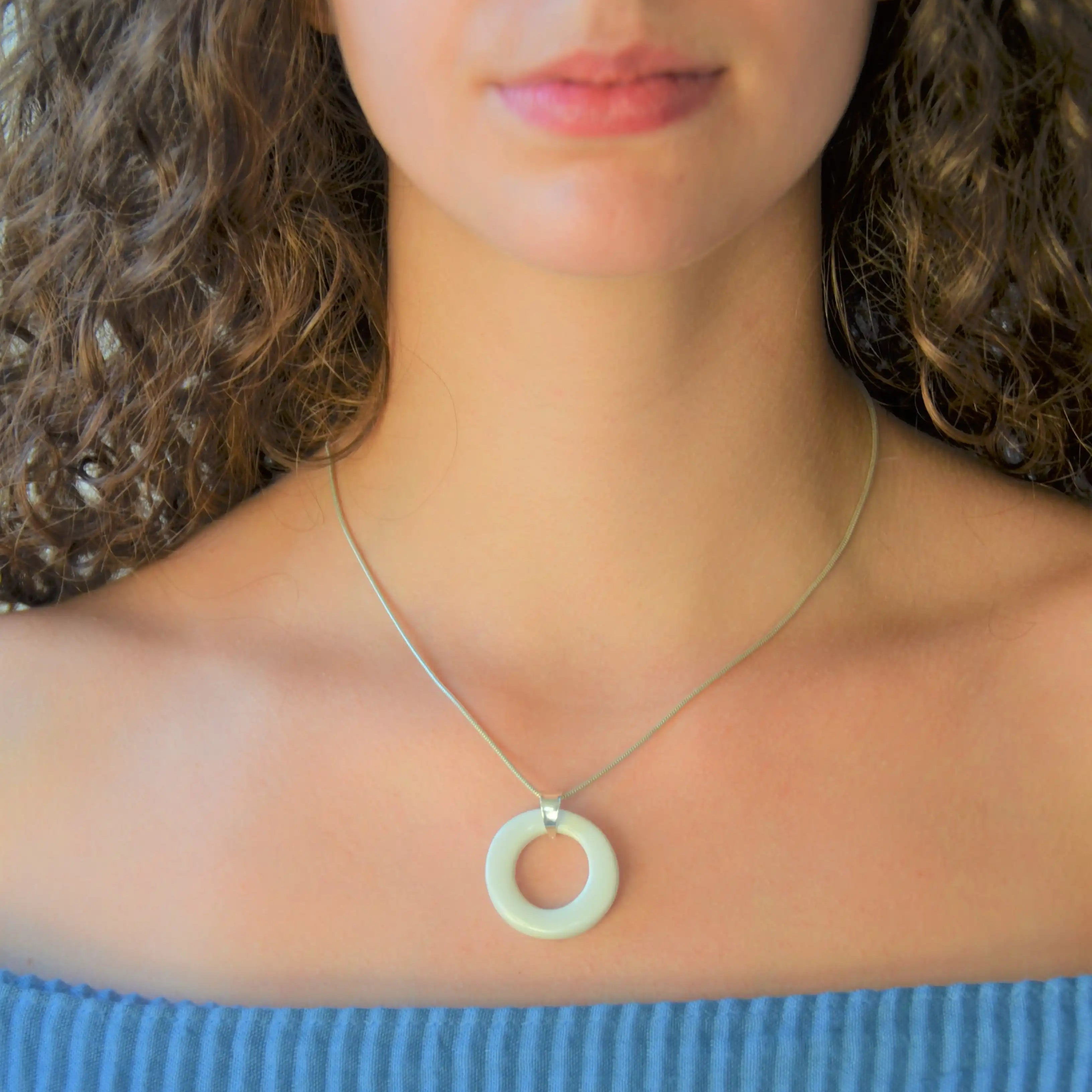 Colgante de cerámica circular blanco sobre superficie natural, joyería artesanal de Maia Cerámica