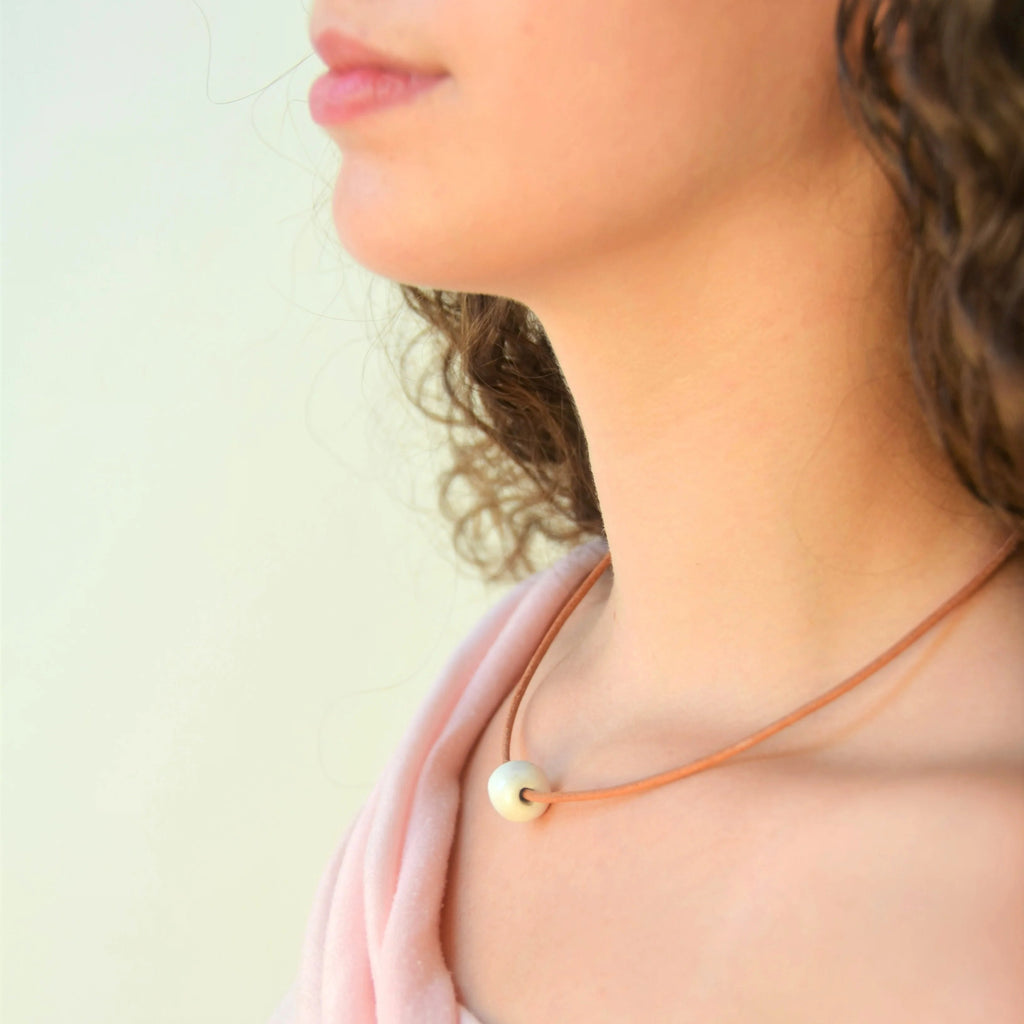 Collar artesanal de cerámica con diseño de esfera en blanco y cordón de cuero con cierre de plata de ley, hecho a mano por Maia Cerámica