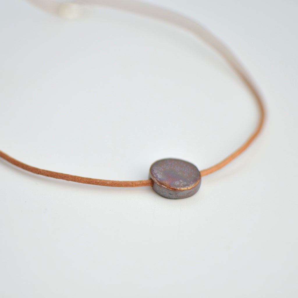 Collar de cerámica luna marrón dorado sobre superficie natural, joyería artesanal hecha a mano por Maia Cerámica