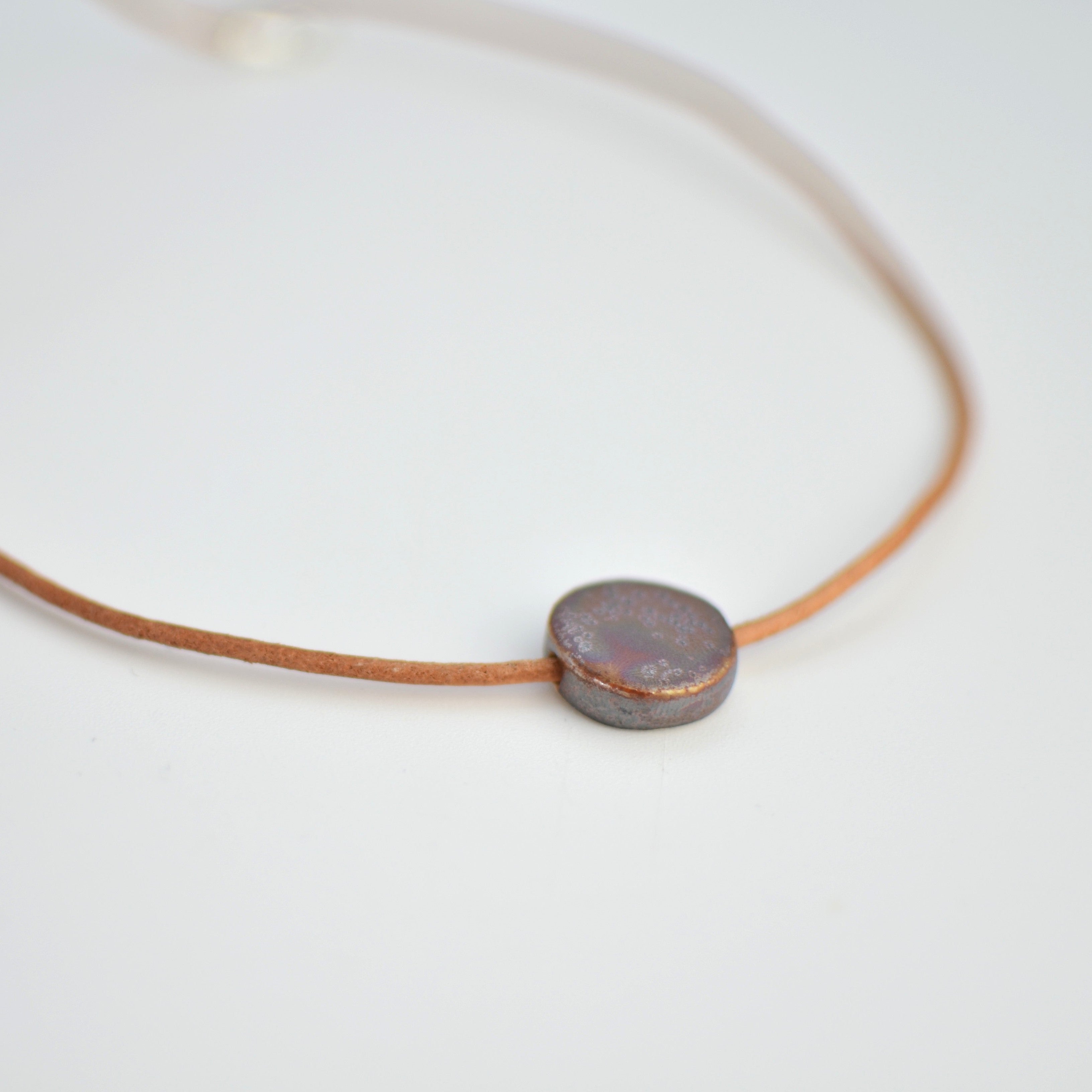 Collar de cerámica luna marrón dorado sobre superficie natural, joyería artesanal hecha a mano por Maia Cerámica