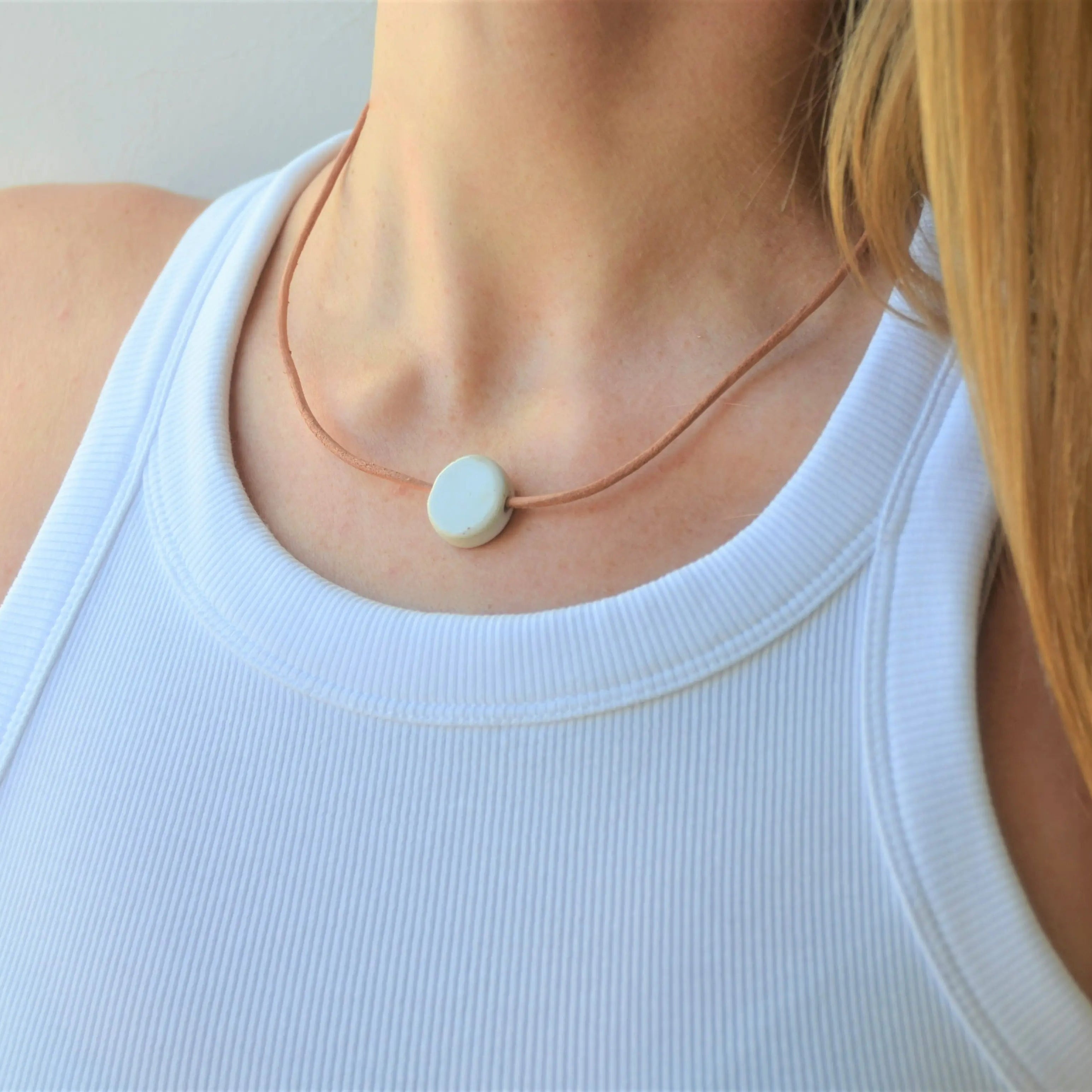Collar artesanal de cerámica con diseño de luna en blanco y cordón de cuero con cierre de plata de ley, hecho a mano por Maia Cerámica