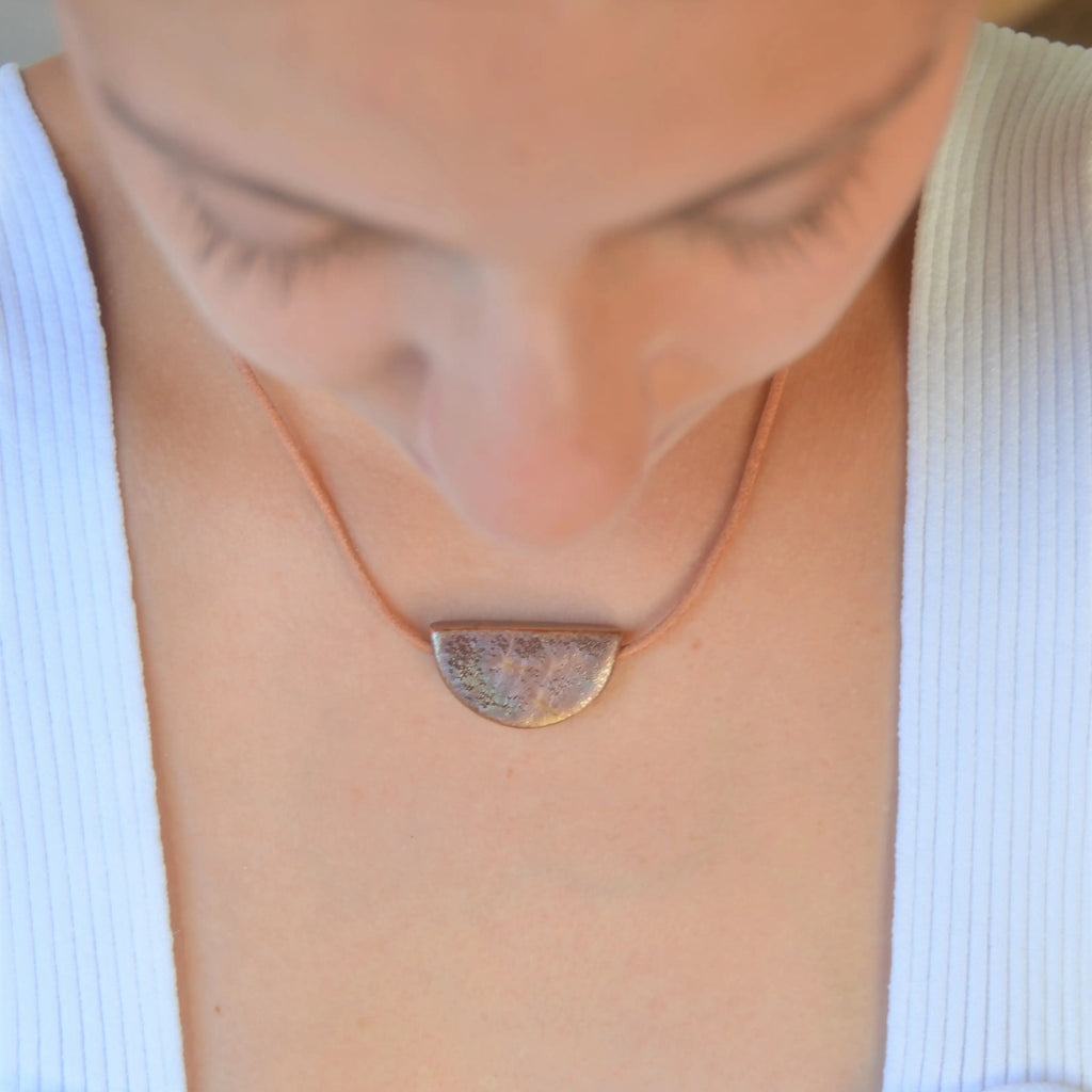 Collar artesanal de cerámica media luna en tono marrón dorado con cordón de cuero, hecho a mano por Maia Cerámica