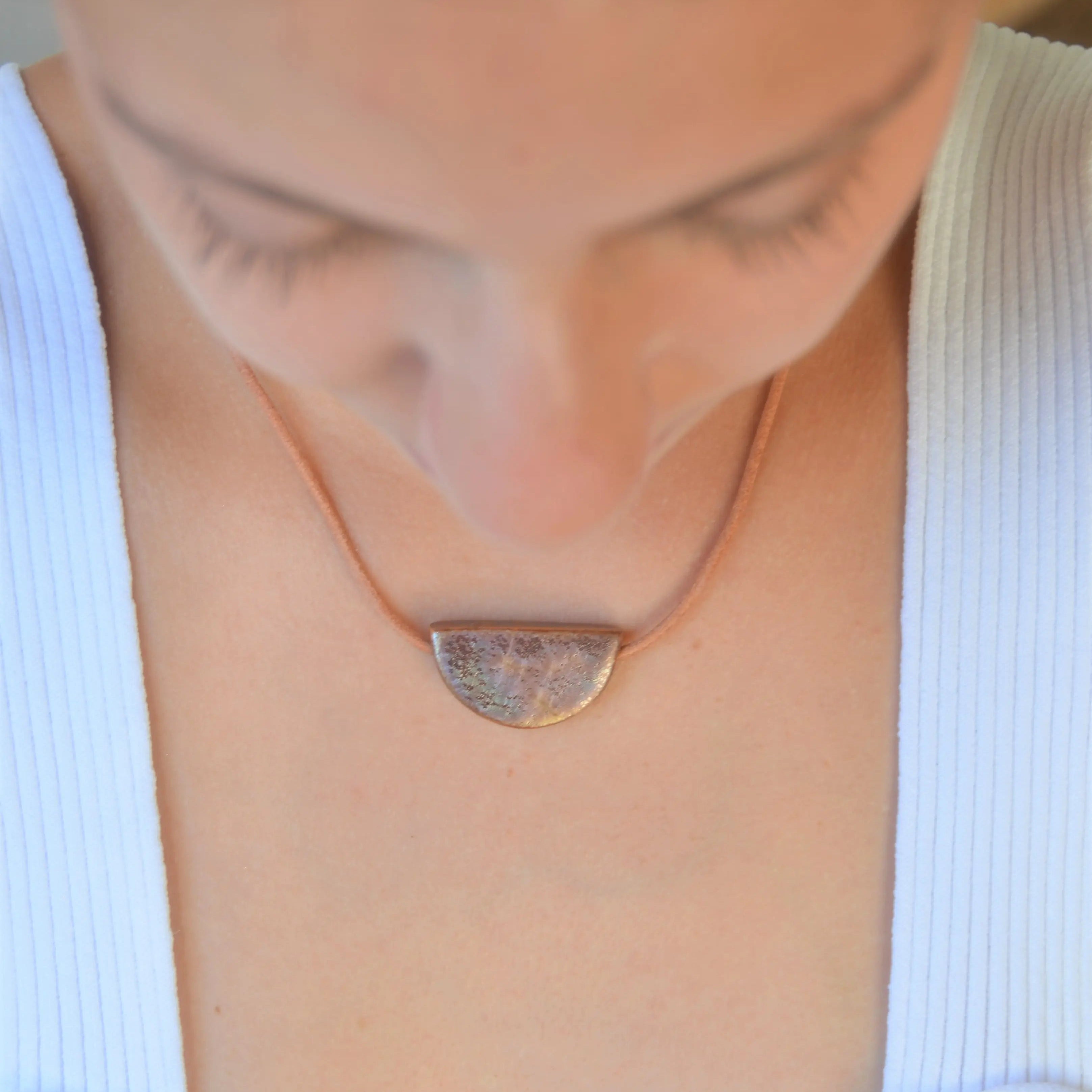 Collar artesanal de cerámica media luna en tono marrón dorado con cordón de cuero, hecho a mano por Maia Cerámica