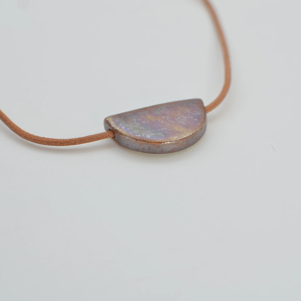 Detalle de collar de cerámica artesanal con colgante de media luna y acabado marrón dorado