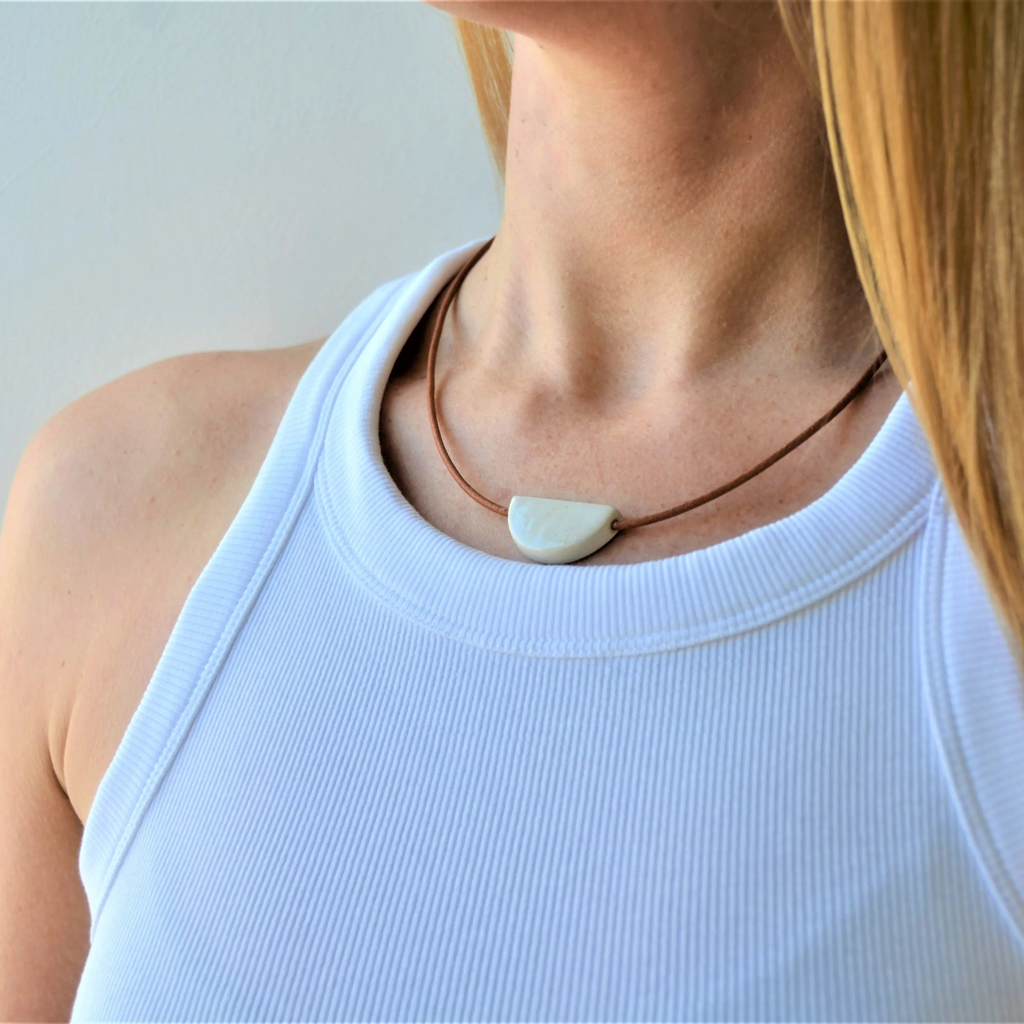 Collar de cerámica media luna blanco sobre superficie natural, pieza artesanal hecha a mano por Maia Cerámica