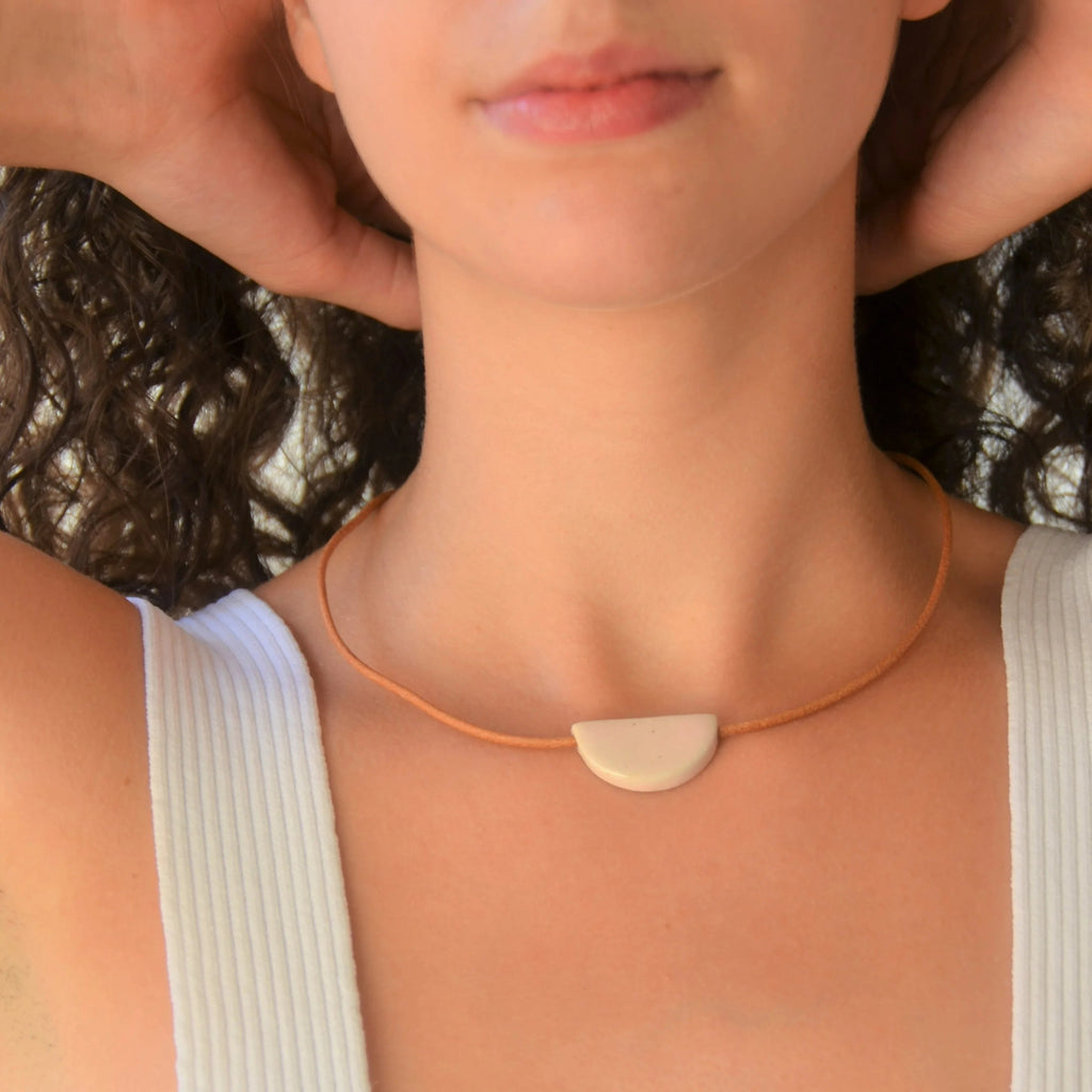 Collar artesanal de cerámica media luna en tono rosa con cordón de cuero y cierre de plata de ley, hecho a mano por Maia Cerámica
