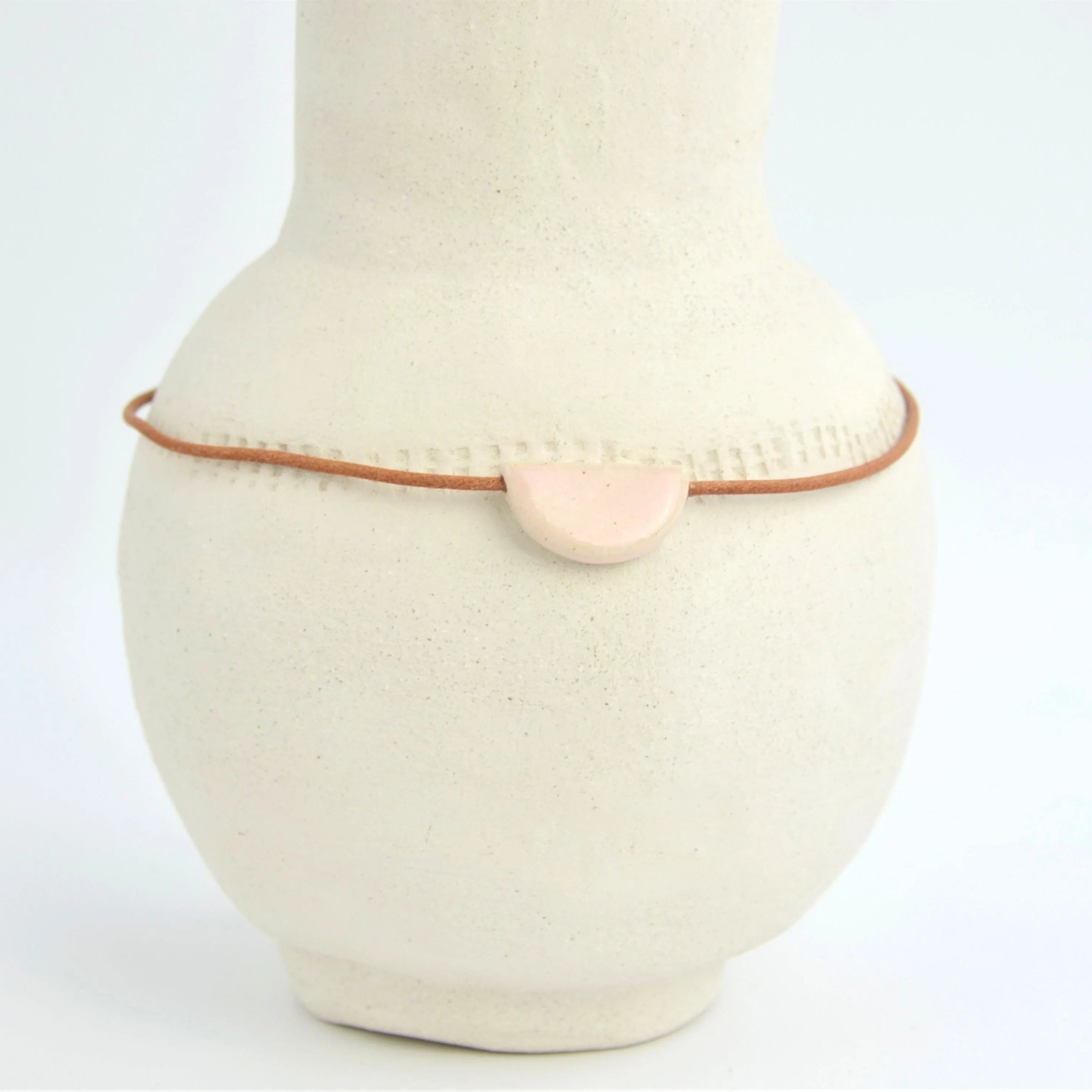 Collar de cerámica media luna rosa sobre superficie natural, joyería artesanal delicada hecha a mano por Maia Cerámica

