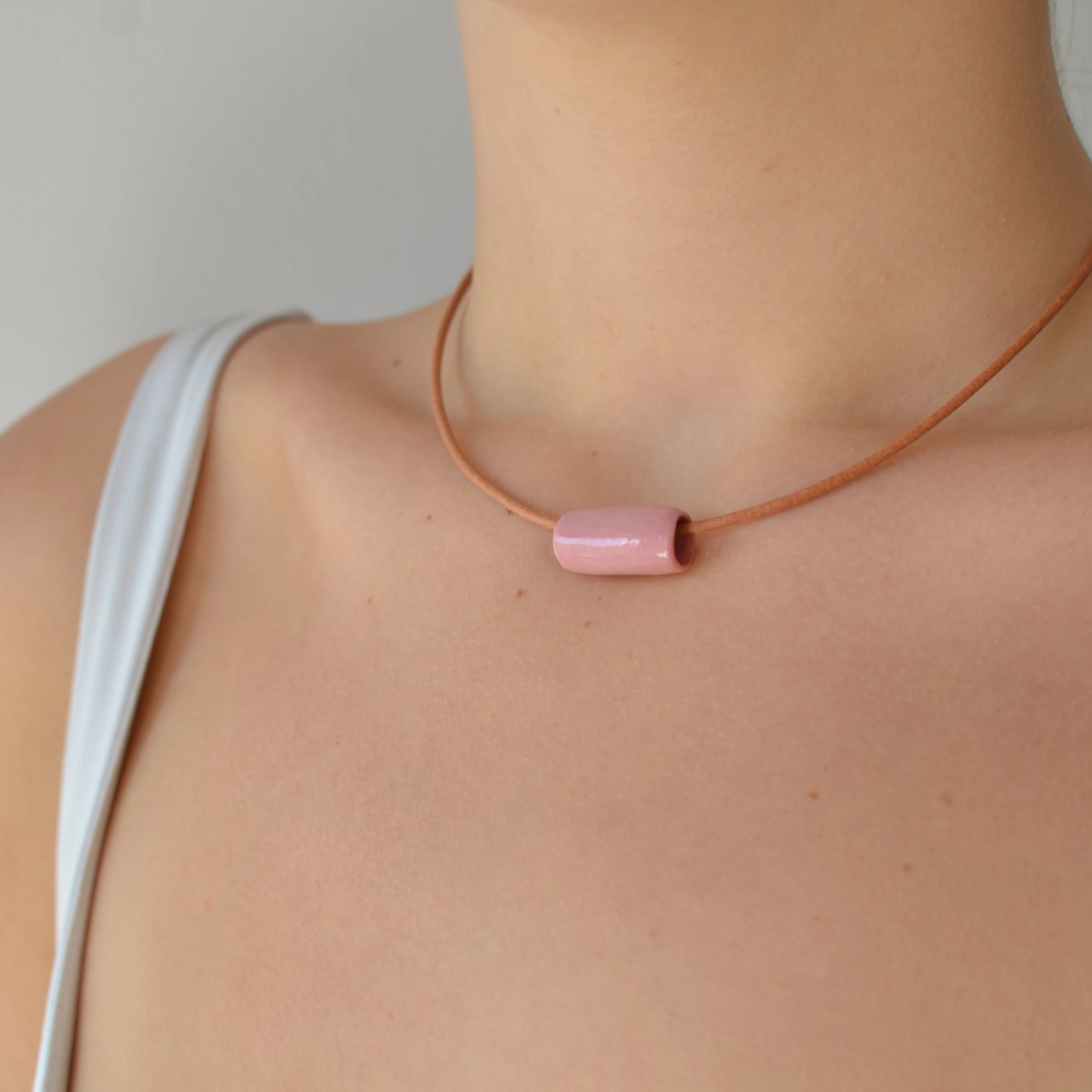 Collar artesanal de cerámica con diseño de tubo en tono rosa, cordón de cuero y cierre de plata de ley, hecho a mano por Maia Cerámica