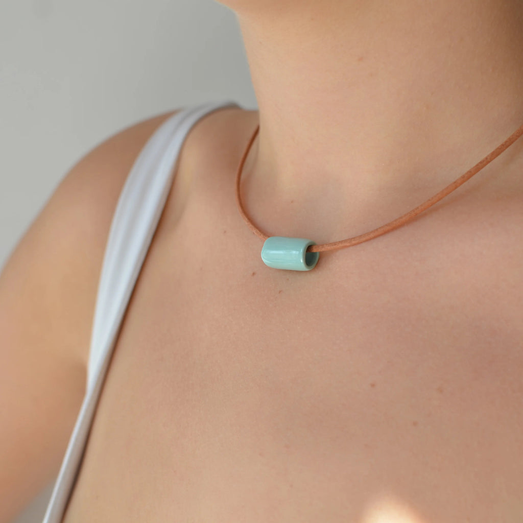 Detalle de collar de cerámica tubo verde menta sobre superficie natural, joyería artesanal única de Maia Cerámica