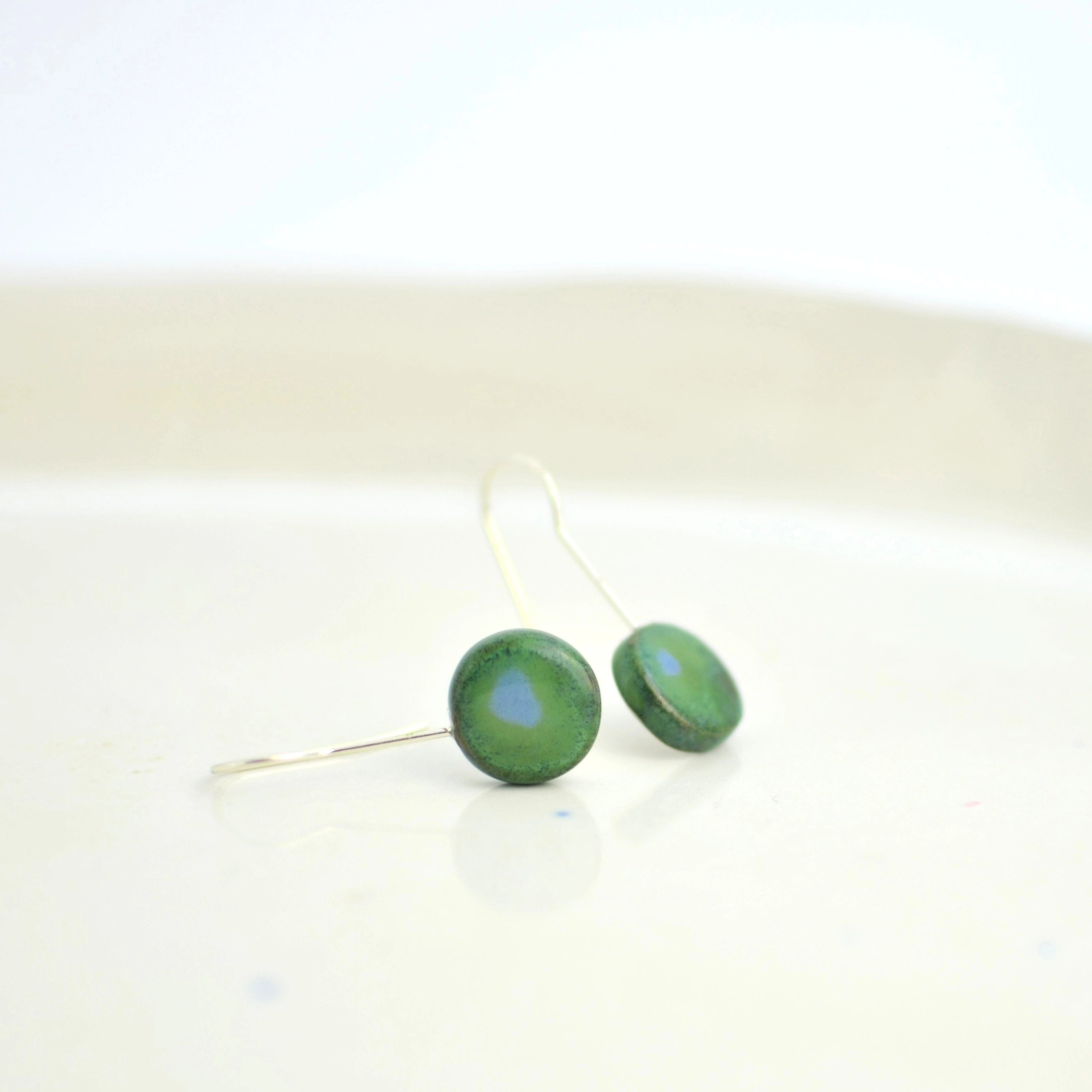 Pendientes de cerámica luna verde azulado sobre superficie natural, joyería artesanal única de Maia Cerámica