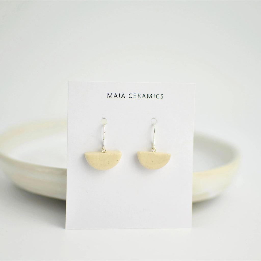 Pendientes de cerámica media luna blanco sobre superficie natural, joyería artesanal única de Maia Cerámica