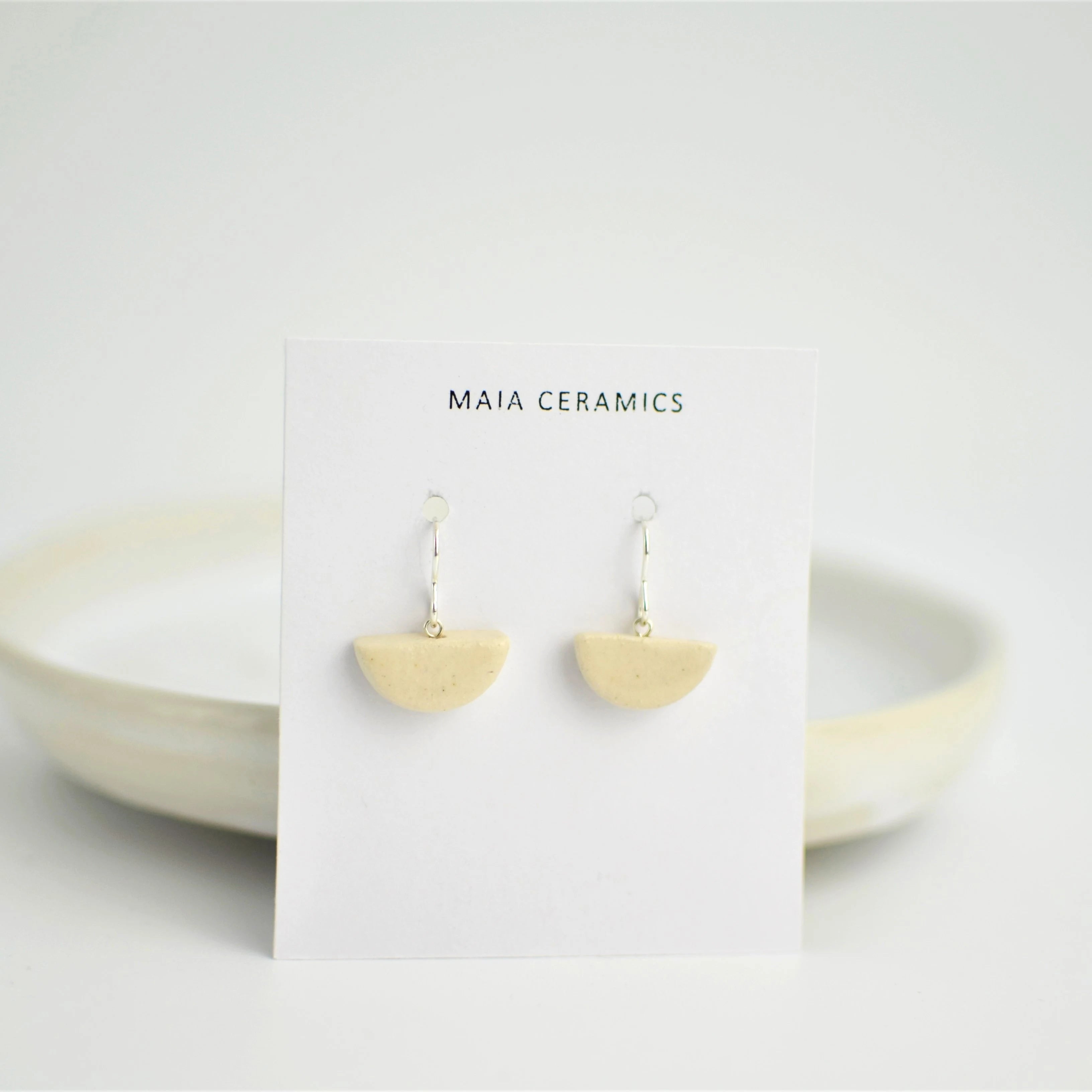 Pendientes de cerámica media luna blanco sobre superficie natural, joyería artesanal única de Maia Cerámica