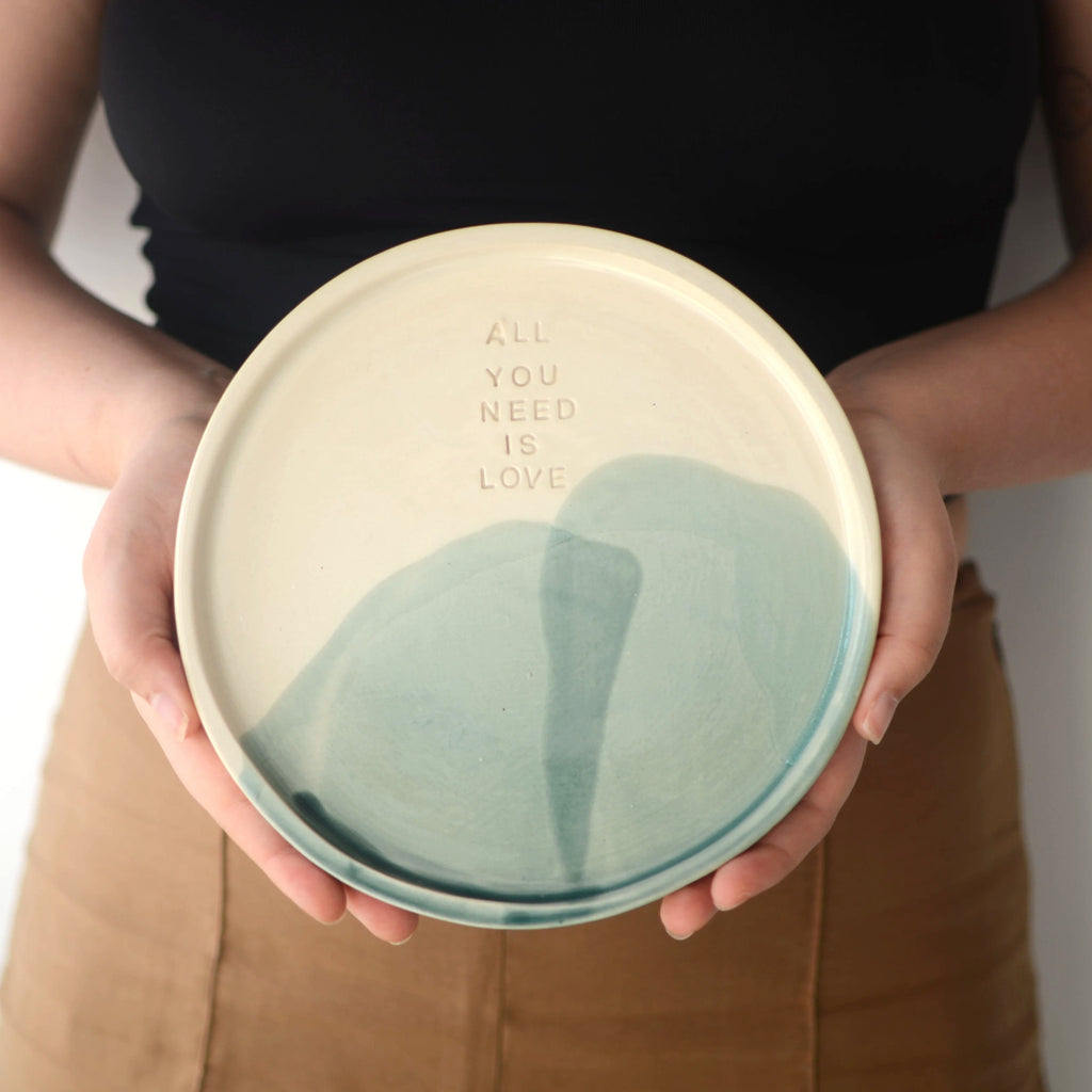 Mano sosteniendo plato cerámica artesanal All You Need Is Love blanco y turquesa hecho a mano 21cm - Maia Artesanía Cerámica