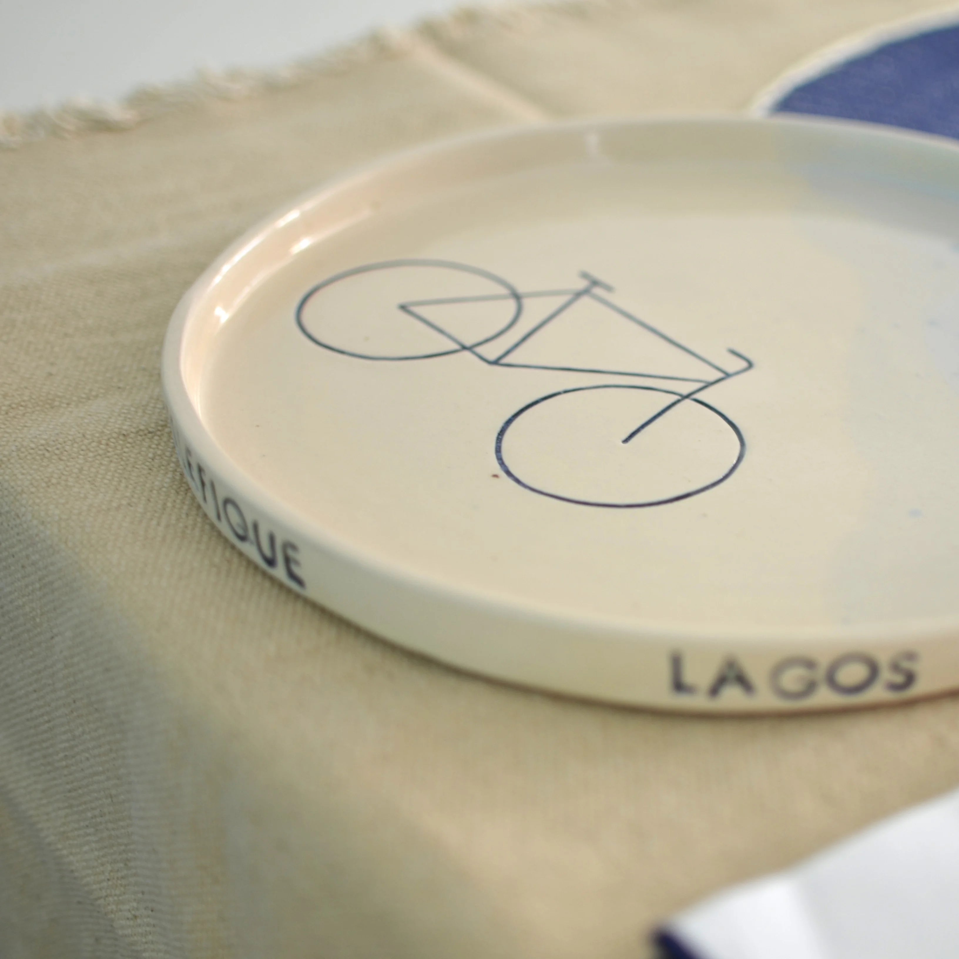 Detalle bicicleta y nombres de lugares en plato cerámica artesanal celeste hecho a mano - Maia Artesanía Cerámica