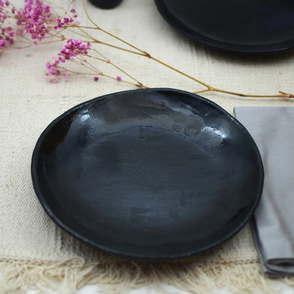 Vista lateral de plato cerámico negro artesanal, forma fluida y orgánica hecho a mano 21cm
