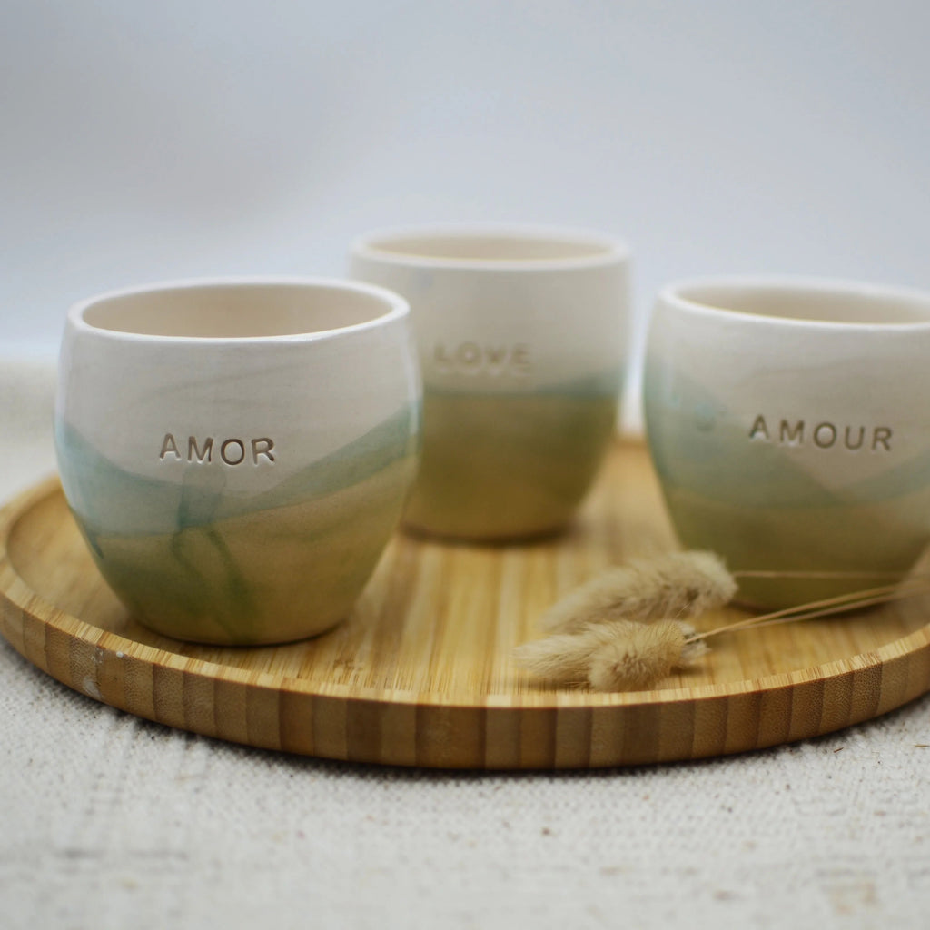 Detalle de vasos de cerámica hechos a mano esmaltados en blanco y turquesa con inscripción Amor Love Amour - Maia Artesanía Cerámica