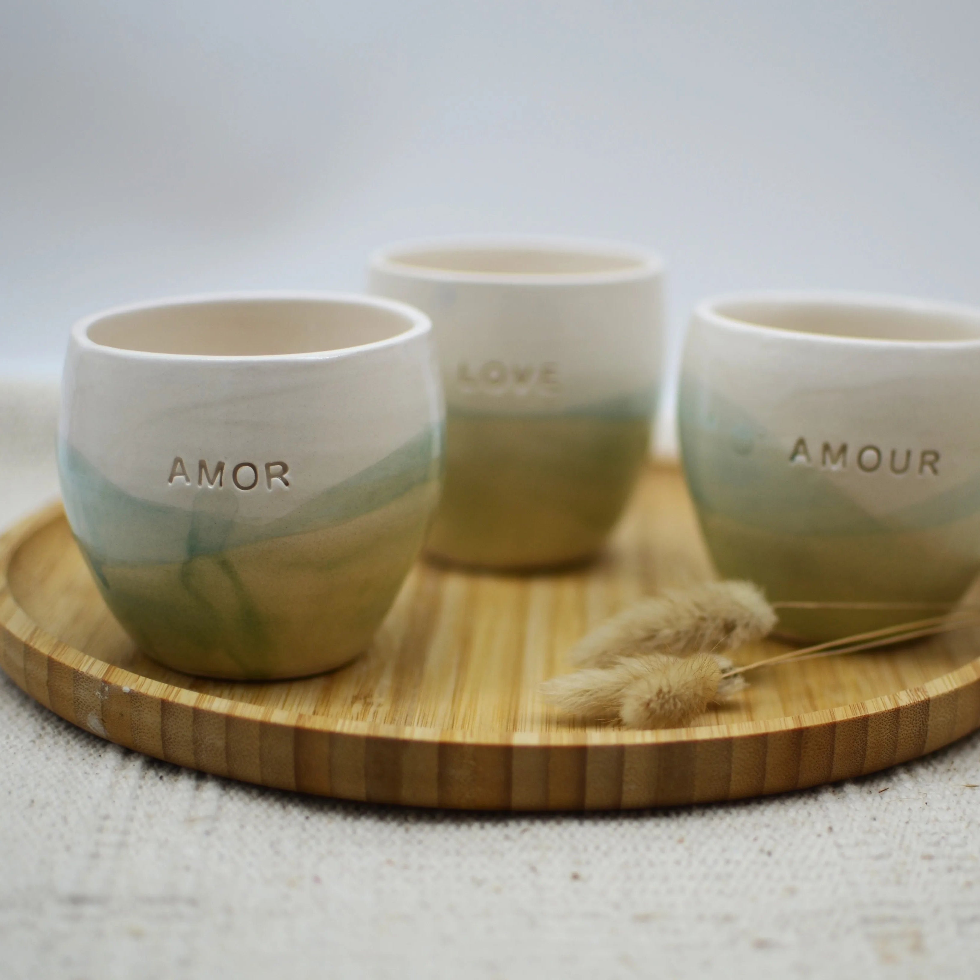 Detalle de vasos de cerámica hechos a mano esmaltados en blanco y turquesa con inscripción Amor Love Amour - Maia Artesanía Cerámica